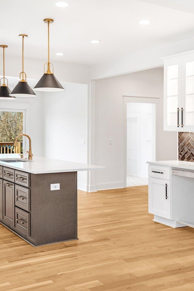 kitchen with hanging light fixtures, sink, white cabinets, and light hardwood / wood-style flooring