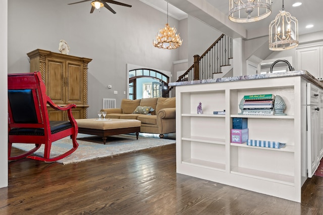 sitting room with dark wood-type flooring, ceiling fan with notable chandelier, and built in shelves