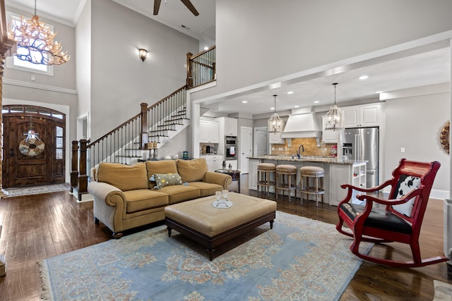 living room with sink, a towering ceiling, ornamental molding, dark hardwood / wood-style flooring, and ceiling fan with notable chandelier