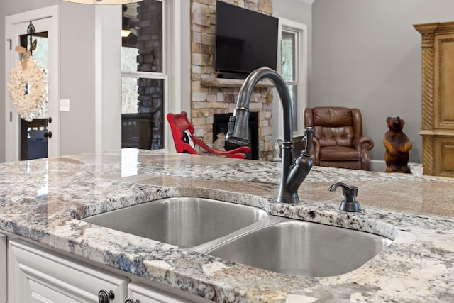 kitchen with light stone counters, a stone fireplace, sink, and white cabinets