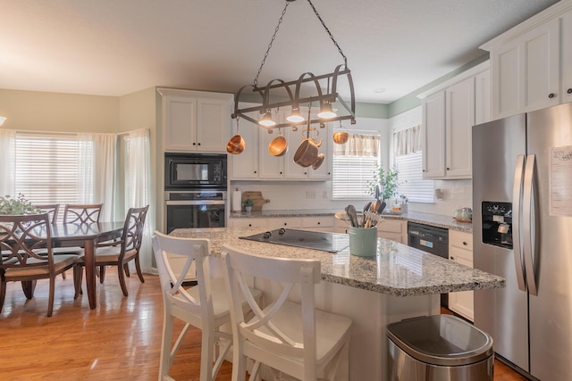 kitchen featuring hanging light fixtures, white cabinets, a kitchen breakfast bar, and black appliances