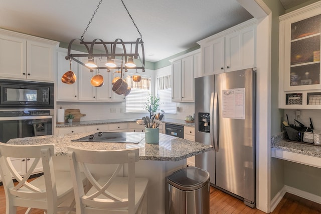 kitchen featuring a breakfast bar area, light hardwood / wood-style flooring, hanging light fixtures, and black appliances