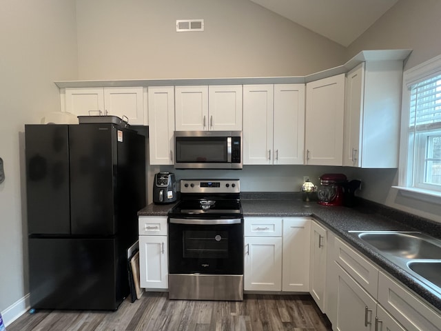 kitchen featuring appliances with stainless steel finishes, vaulted ceiling, hardwood / wood-style floors, and white cabinets