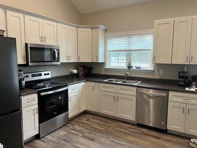 kitchen featuring vaulted ceiling, appliances with stainless steel finishes, dark hardwood / wood-style floors, sink, and white cabinets