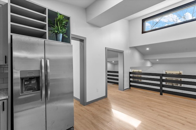 kitchen featuring light wood-type flooring, a towering ceiling, baseboards, and stainless steel fridge with ice dispenser