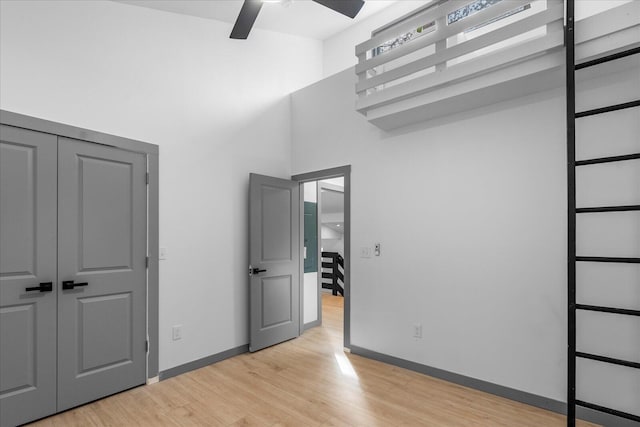 unfurnished bedroom with a ceiling fan, light wood-type flooring, a towering ceiling, and baseboards