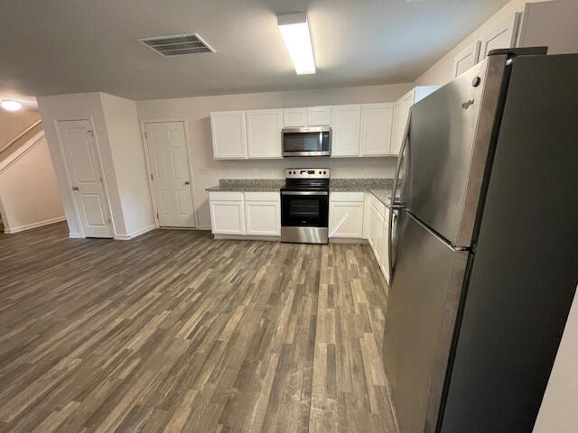 kitchen with appliances with stainless steel finishes, white cabinets, and dark hardwood / wood-style flooring