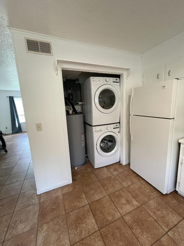 washroom with stacked washer and dryer, dark tile patterned floors, water heater, and a textured ceiling