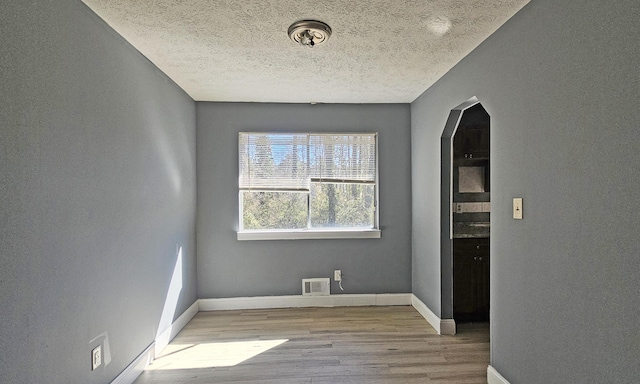 spare room with a textured ceiling and light hardwood / wood-style floors