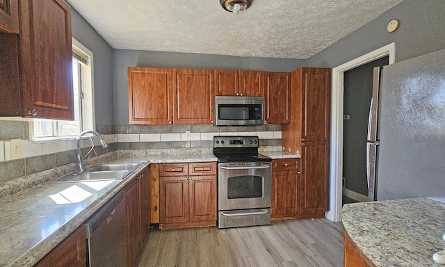 kitchen featuring sink, light hardwood / wood-style flooring, a textured ceiling, and appliances with stainless steel finishes