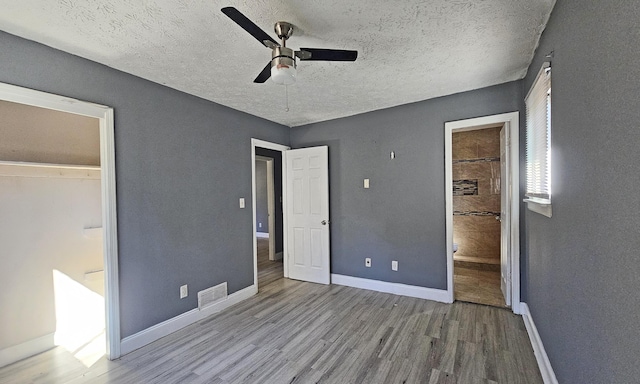 unfurnished bedroom featuring wood-type flooring, ensuite bathroom, ceiling fan, and a textured ceiling