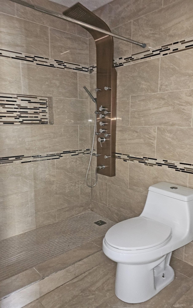 bathroom with a tile shower, tile walls, and toilet