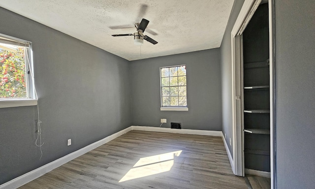 spare room featuring ceiling fan, light hardwood / wood-style floors, a textured ceiling, and a wealth of natural light