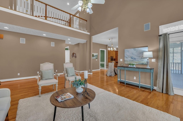 living room with hardwood / wood-style flooring, ceiling fan with notable chandelier, and a high ceiling