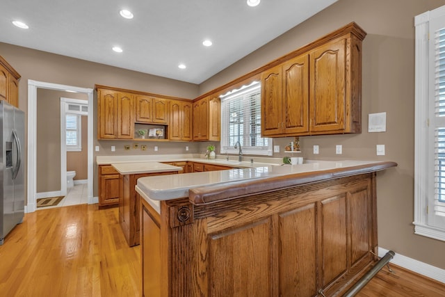 kitchen with sink, stainless steel fridge, kitchen peninsula, and light wood-type flooring