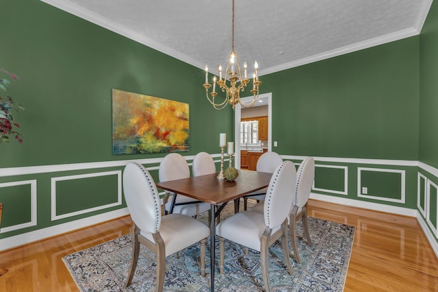 dining space with an inviting chandelier, ornamental molding, wood-type flooring, and a textured ceiling