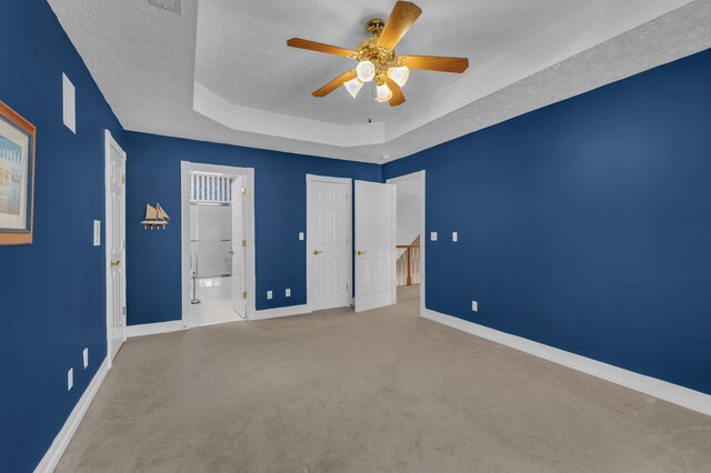 unfurnished bedroom featuring connected bathroom, light carpet, a textured ceiling, a raised ceiling, and ceiling fan