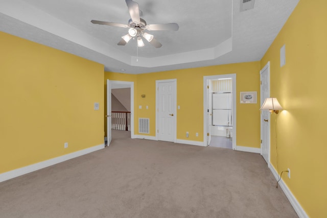 unfurnished bedroom with a tray ceiling, a textured ceiling, light colored carpet, and ceiling fan