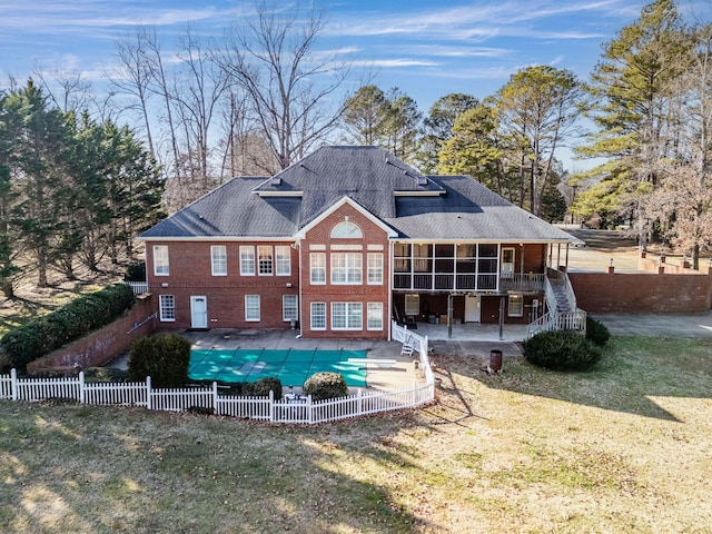 rear view of property featuring a yard, a patio area, a sunroom, and a covered pool