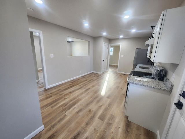 kitchen featuring light stone counters, light hardwood / wood-style floors, stainless steel refrigerator, and white cabinets