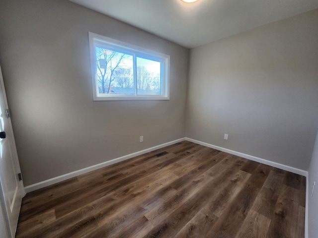 spare room featuring visible vents, baseboards, and dark wood-style flooring