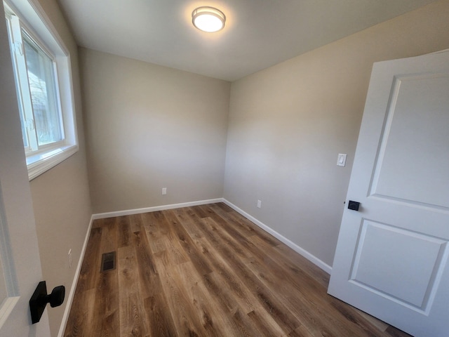 empty room with wood finished floors, visible vents, and baseboards