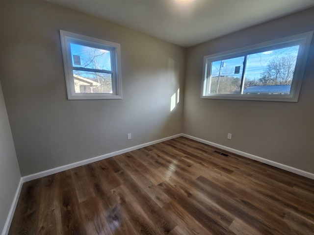 unfurnished room with dark wood-type flooring, visible vents, and baseboards