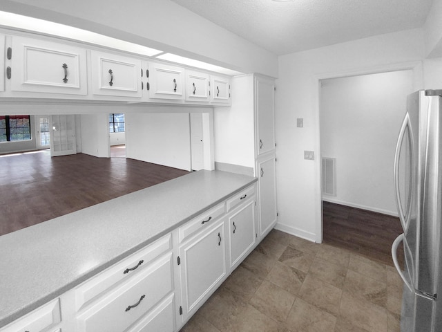 kitchen with stainless steel fridge, a textured ceiling, and white cabinets