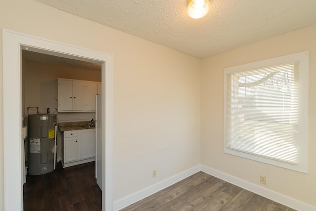 spare room with water heater, dark wood-type flooring, and a textured ceiling