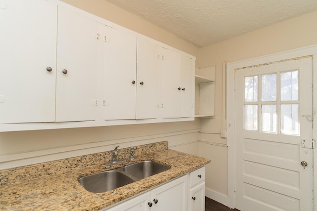 kitchen featuring white cabinetry, sink, light stone countertops, and a textured ceiling