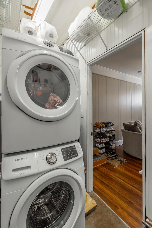 laundry area with dark wood-type flooring, stacked washer and clothes dryer, and wood walls