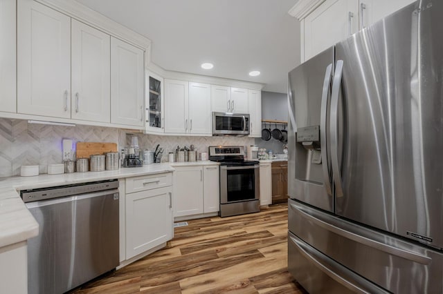 kitchen featuring white cabinetry, backsplash, light wood-type flooring, and appliances with stainless steel finishes