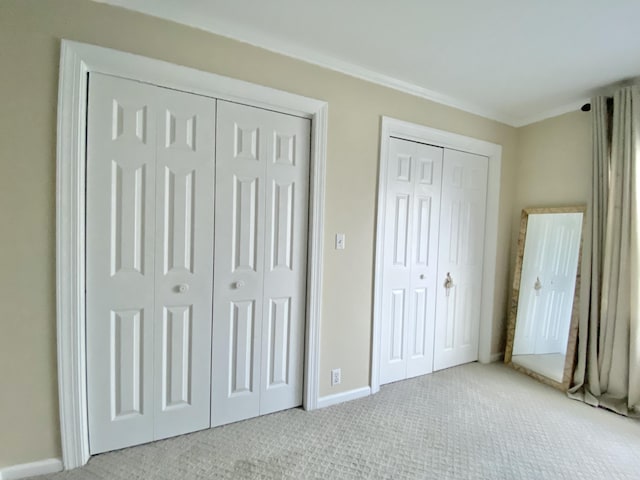 unfurnished bedroom featuring light carpet, two closets, and crown molding