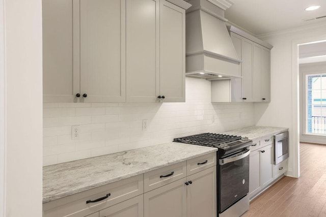 kitchen featuring light hardwood / wood-style flooring, premium range hood, stainless steel appliances, light stone countertops, and decorative backsplash