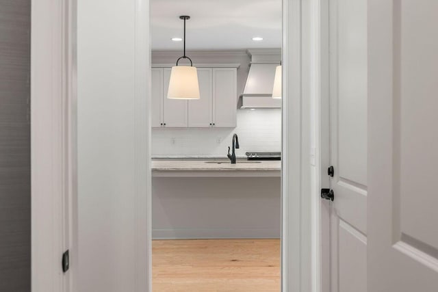 kitchen featuring premium range hood, sink, hanging light fixtures, light hardwood / wood-style floors, and decorative backsplash