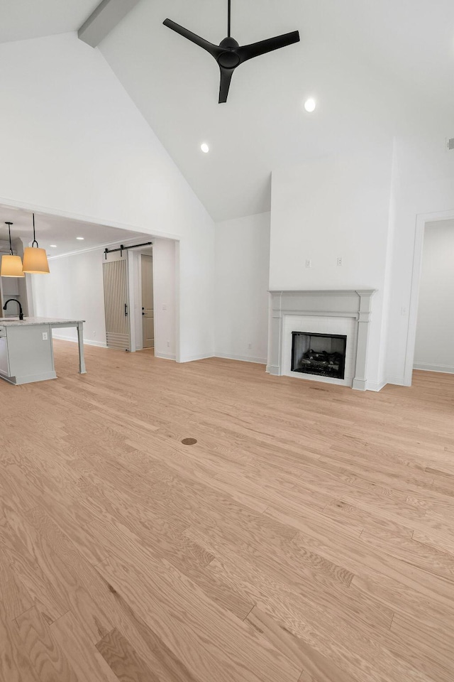 unfurnished living room featuring high vaulted ceiling, beamed ceiling, sink, ceiling fan, and light wood-type flooring