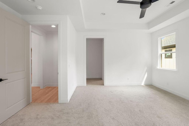 spare room featuring ceiling fan, light colored carpet, and a raised ceiling