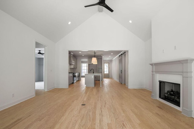 unfurnished living room with lofted ceiling, sink, ceiling fan, and light hardwood / wood-style flooring