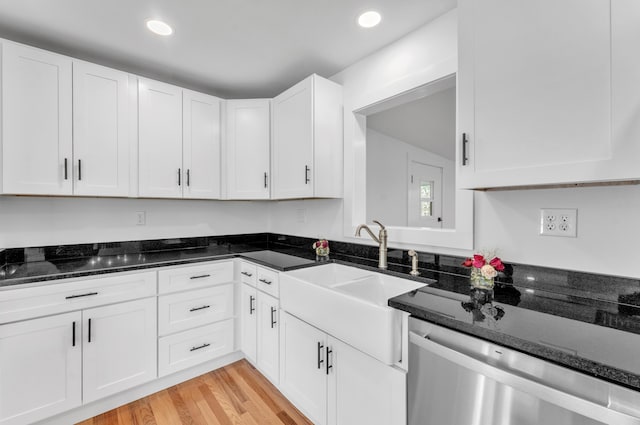 kitchen with light wood-style flooring, stainless steel dishwasher, white cabinets, a sink, and dark stone counters