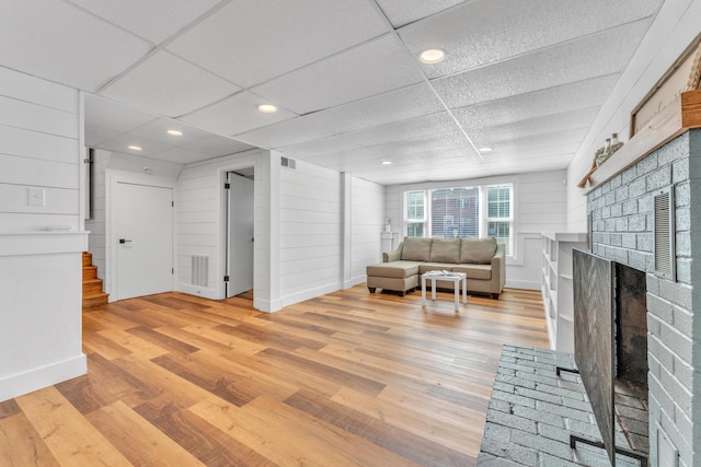 unfurnished living room with visible vents, a drop ceiling, stairs, light wood-type flooring, and a fireplace