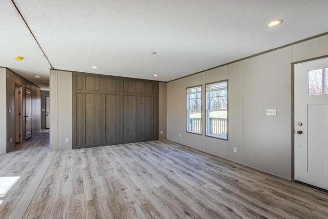 interior space with crown molding, wooden walls, a textured ceiling, and light wood-type flooring