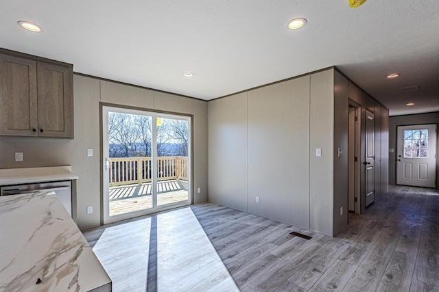 kitchen with light stone counters, ornamental molding, dishwasher, and light hardwood / wood-style floors