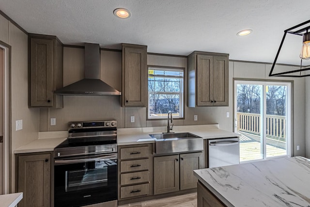 kitchen with appliances with stainless steel finishes, wall chimney exhaust hood, sink, and a textured ceiling