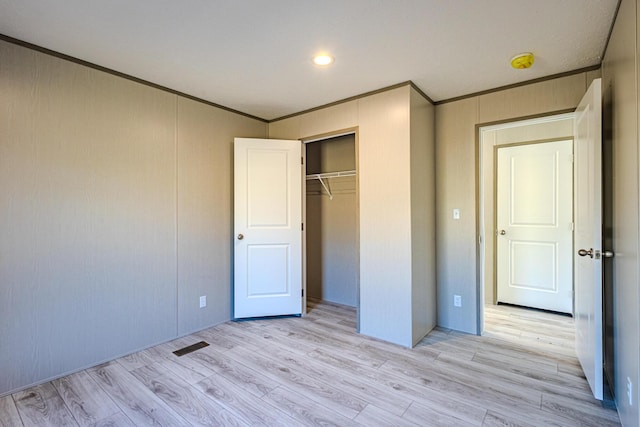 unfurnished bedroom with crown molding, light hardwood / wood-style floors, and a closet