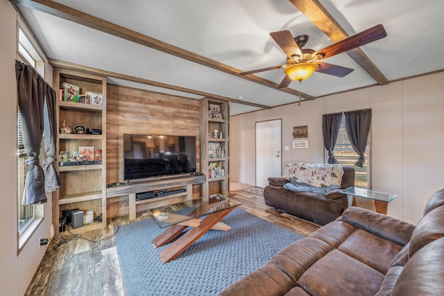 living room featuring beamed ceiling, ceiling fan, wood-type flooring, and a textured ceiling