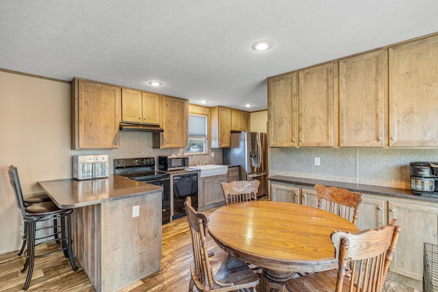 kitchen featuring sink, a breakfast bar area, backsplash, black appliances, and light wood-type flooring