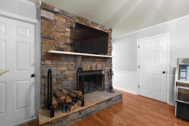 living room featuring crown molding, a stone fireplace, hardwood / wood-style floors, and a textured ceiling