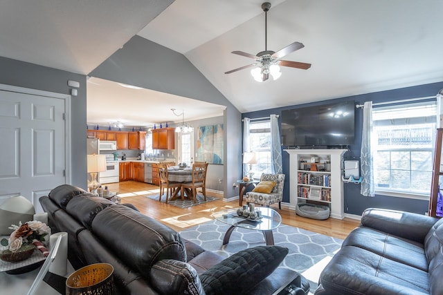 living room with lofted ceiling, ceiling fan with notable chandelier, plenty of natural light, and light wood-type flooring