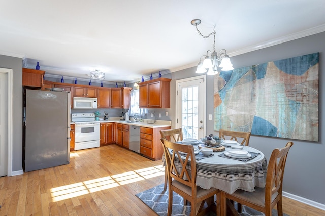 kitchen featuring sink, decorative light fixtures, ornamental molding, appliances with stainless steel finishes, and light hardwood / wood-style floors