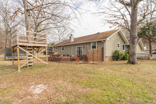 rear view of property with a wooden deck, a yard, and a trampoline